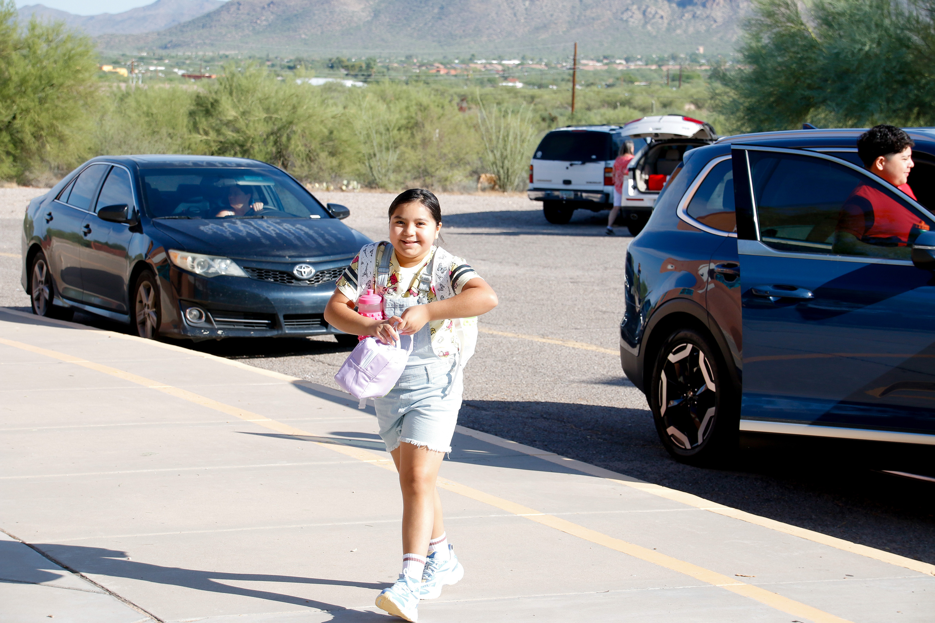 A girl smiles as she walks from the parking lot on the first day of school