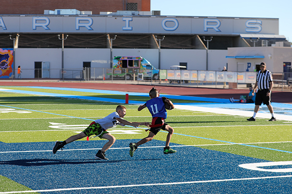 A boy in a gray shirt dives for a boy in a blue jersey holding the football