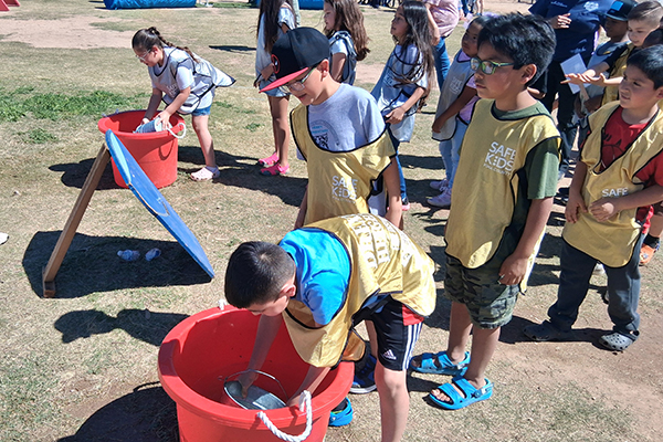 Students fill small buckets of water from large red buckets