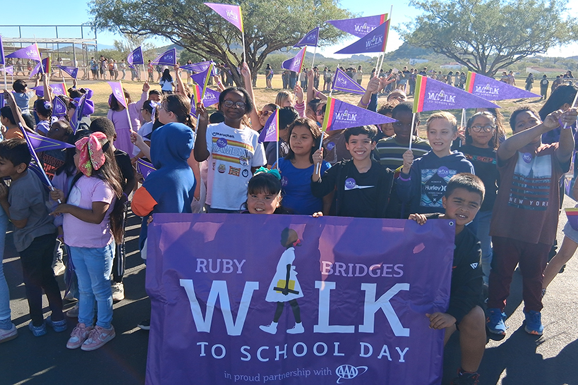 Students hold up a purple Ruby Bridges Walk to School Day banner and purple pennants
