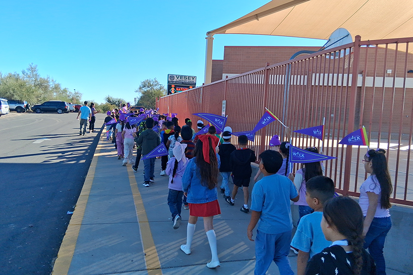 Students walk by the playground, holding up their purple Ruby Bridges pennants