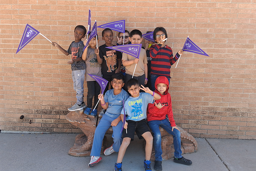 Students pose in front of a brick wall with their purple Ruby Bridges pennants
