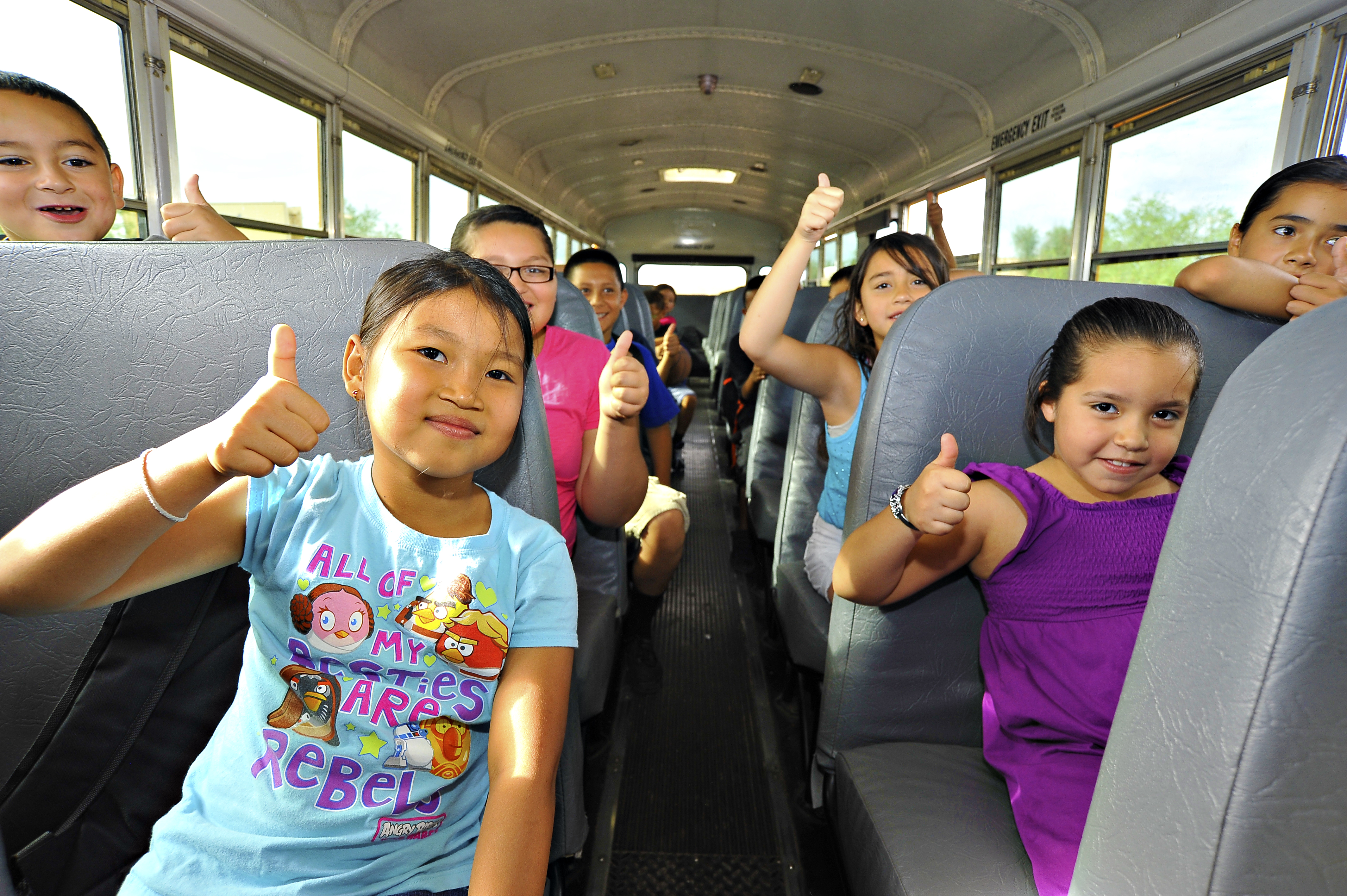 Students smile and give a thumbs up while riding the bus to school